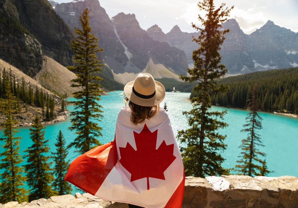 Traveler overlooking a scenic lake in Canada with Canadian flag – Canada Tour Package From India