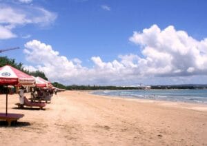 Scenic view of a sandy beach in Bali with umbrellas and clear skies – Bali Tour Package from Delhi