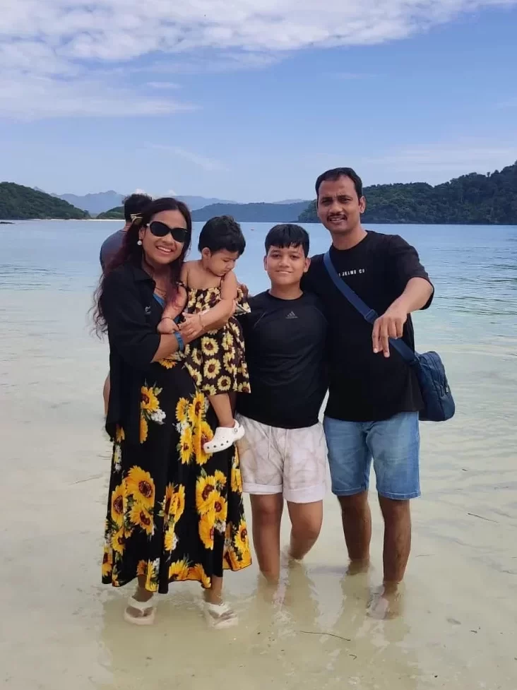 Smiling family of four enjoying a beach day in Singapore, with clear waters and green islands in the background, during their trip organized by Fab Holidays.