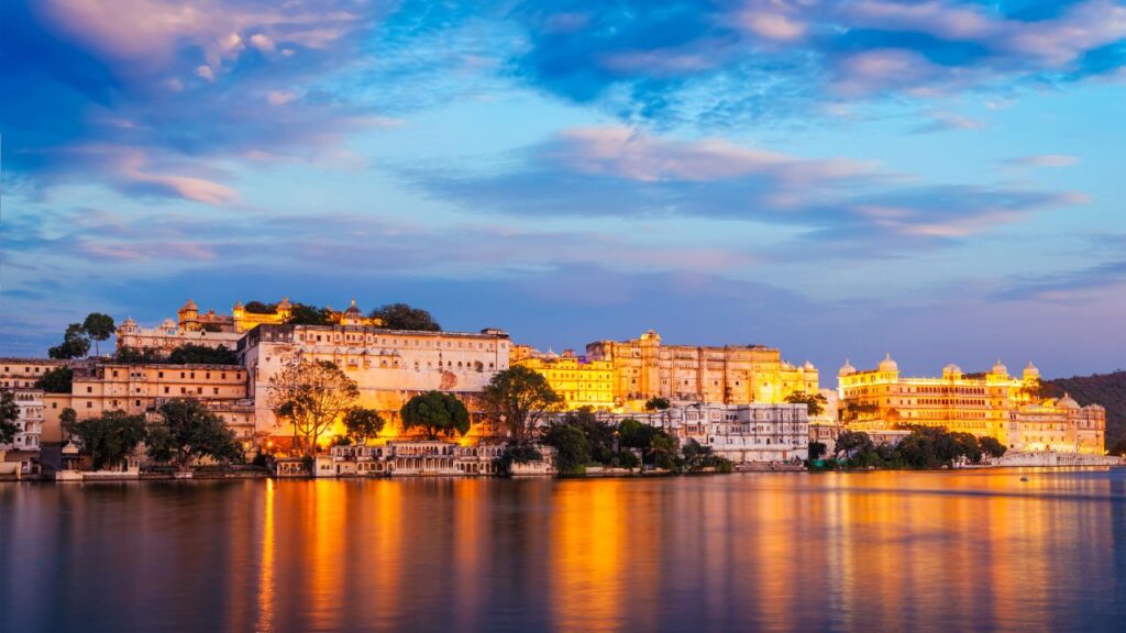 Romantic evening view of Udaipur City Palace by the lake – one of the best honeymoon places in India in December by Fab Holidays.