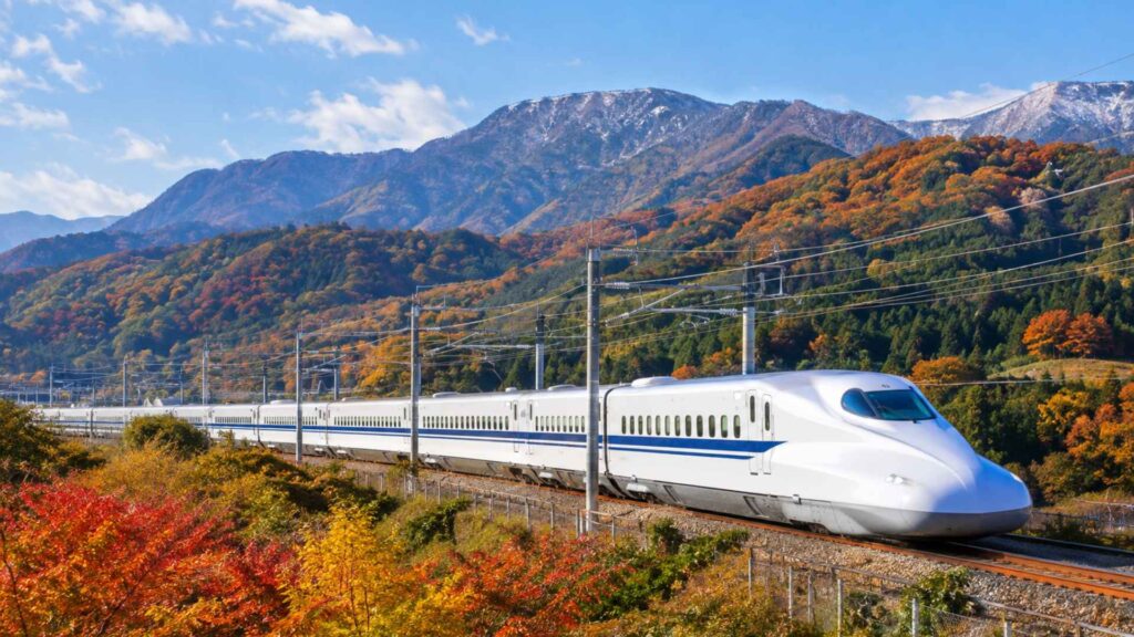 Shinkansen bullet train passing autumn-colored mountains and snow-capped peaks in Japan, useful for planning Japan autumn foliage 2026 travel — Fab Holidays, Best Travel Agency in Delhi